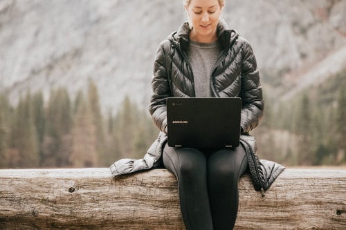 Kobieta siedzi na pniu drzewa z laptopem na kolanach