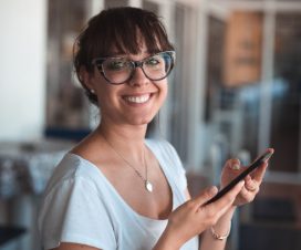 Uśmiechnięta kobieta w okularach z telefonem komórkowym w dłoni